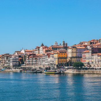 A wide shot of boats on the body of water near houses and buildings in Porto, Portugal